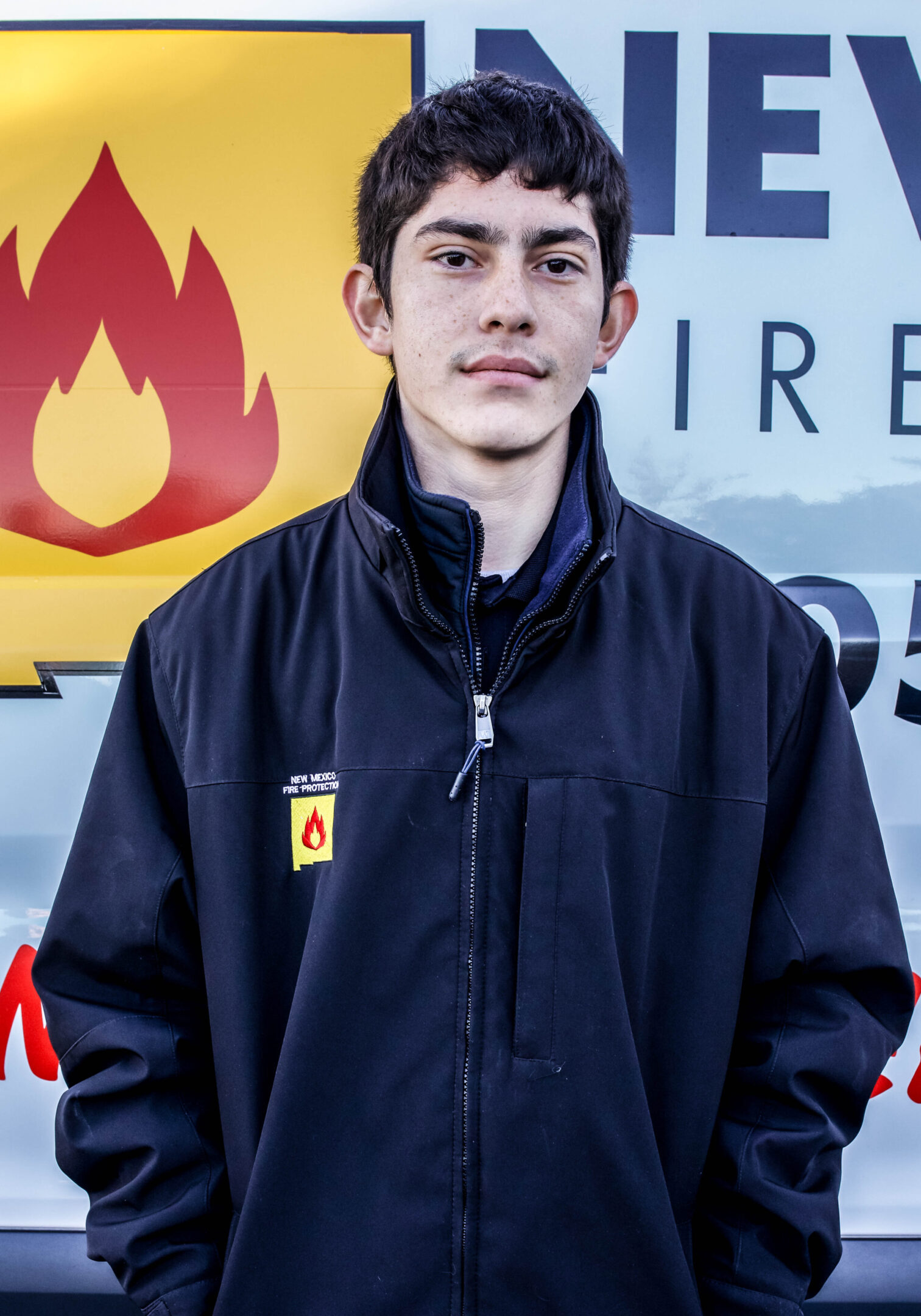 A young man standing in front of a fire station.