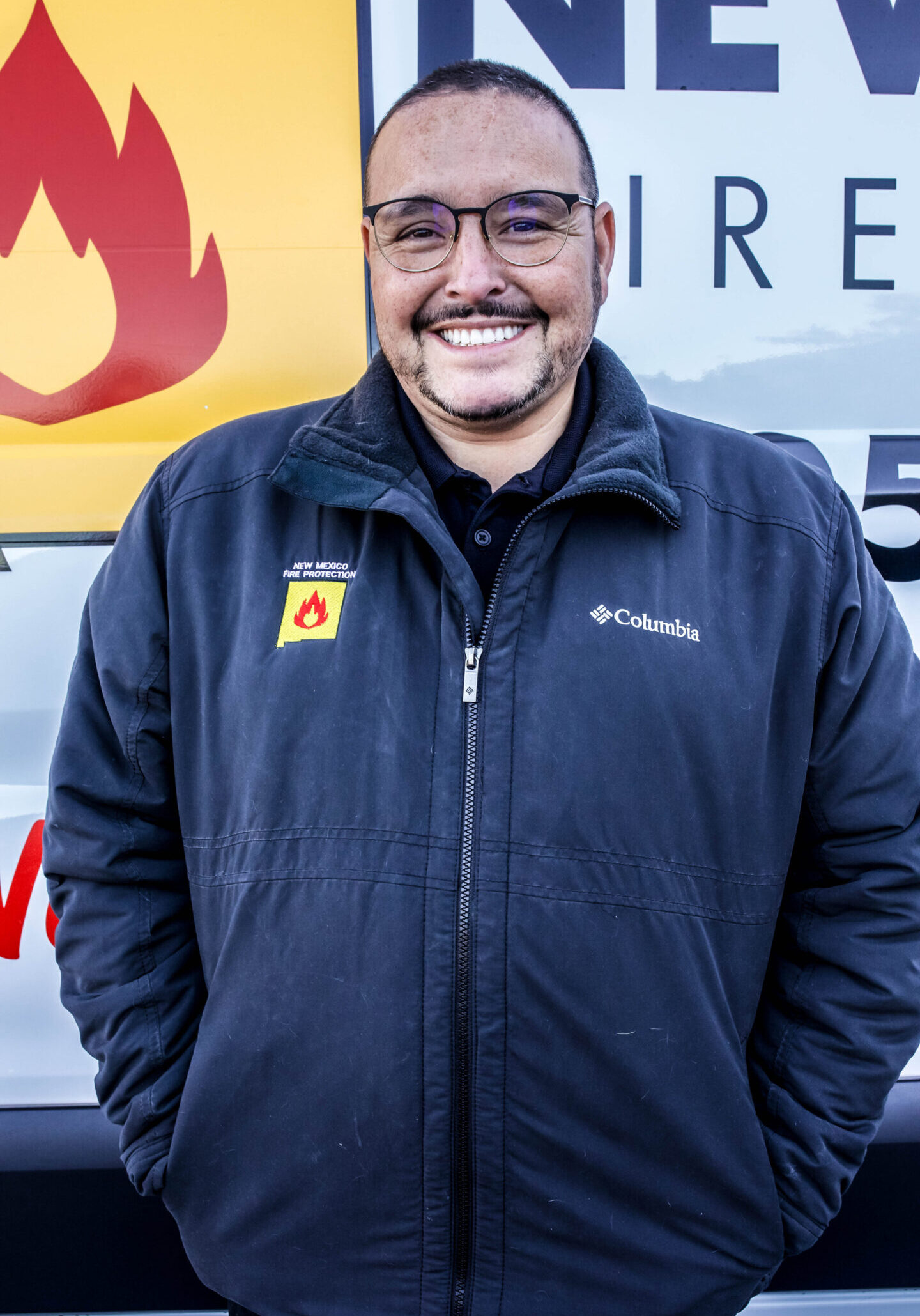 A man in glasses and a jacket standing next to a fire truck.